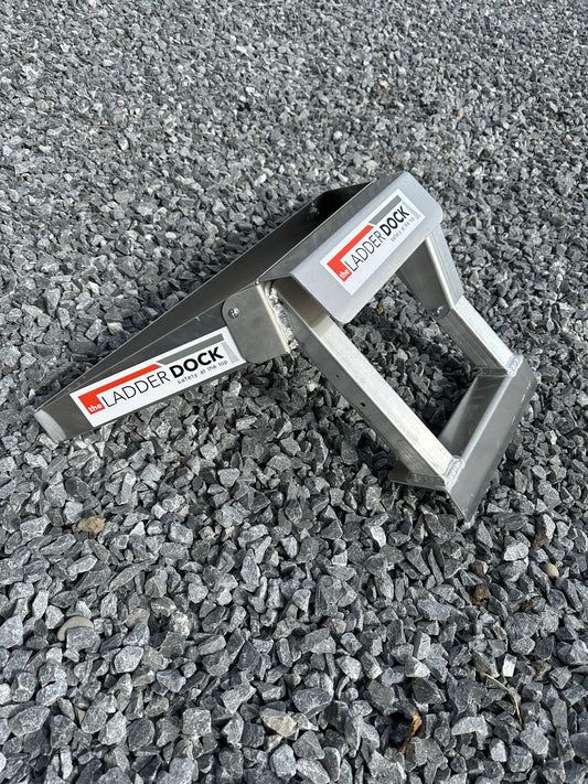 A gray ladder attachment with red and white branding on a gravel surface.